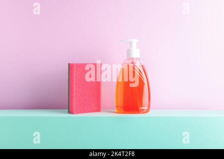 Front view of red dish washing liquid and foam sponge on decorative colored podium. Household conceptual still life, studio shot, copy space. Stock Photo