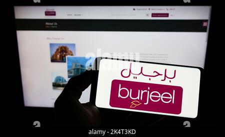 Person holding smartphone with logo of Emirati hospital operator Burjeel on screen in front of company website. Focus on phone display. Stock Photo