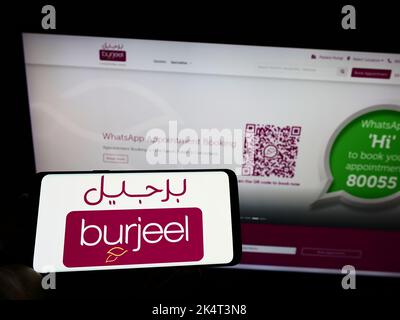 Person holding cellphone with logo of Emirati hospital operator Burjeel on screen in front of business webpage. Focus on phone display. Stock Photo