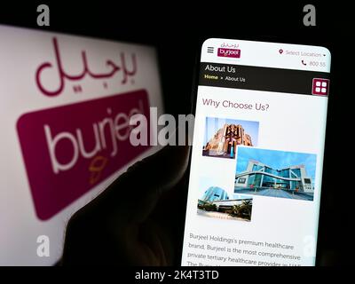 Person holding smartphone with website of Emirati hospital operator Burjeel on screen in front of logo. Focus on center of phone display. Stock Photo