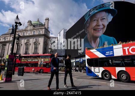 With advertising suspended, visitors and tourists at Piccadilly Circus interact below a colour image of Queen Elizabeth II which is on display on the large scale advertising screens on the day following her death on 9th September 2022 in London, United Kingdom. The Queen, who was 96 reigned as monarch of the UK and Commonwealth for 70 years. Stock Photo