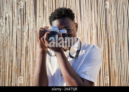 Close up portrait of photographer using an analog camera to take a photo when captured. Young African man with afro holding a vintage camera. Isolated Stock Photo