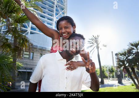 Cheerful portrait of young mixed race couple on holidays on an island. African man giving piggyback. Stock Photo
