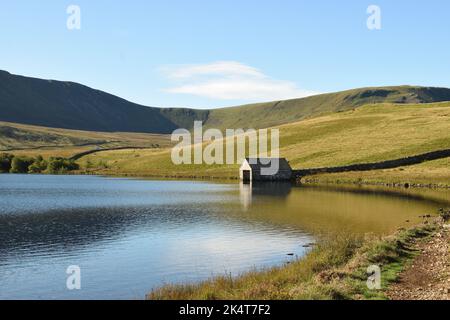 A small boathouse stands on the edge of the shimmering waters of one of the Cregennan Lakes. Snowdonia National Park, Wales, UK. Stock Photo