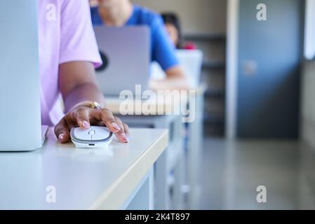 Close up of dark skin hand using computer mouse at classroom, unrecognizable girl and colleagues. Stock Photo