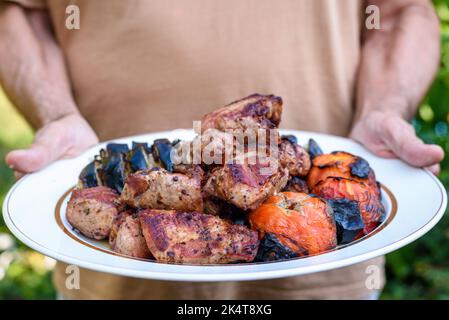 Man holds plate with meat and vegetables roasted on grill Stock Photo
