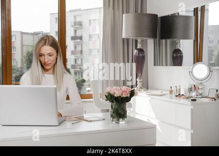 Woman works at the reception in a beauty salon. Typing something on laptop and talks on the phone with client, making appointments in studio Stock Photo
