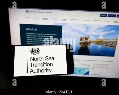 Person holding cellphone with logo of British North Sea Transition Authority (NSTA) on screen in front of webpage. Focus on phone display. Stock Photo