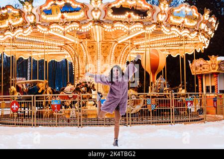 A young girl jumps around a French carousel in an amusement park in winter Stock Photo