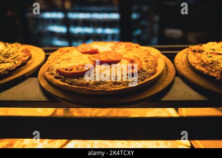 perspective view closeup of different kinds of pizza on wooden plates on the shelves of street food shop window Stock Photo