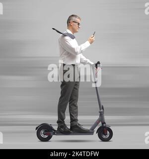 Distracted businessman using his smartphone while riding an electric scooter Stock Photo