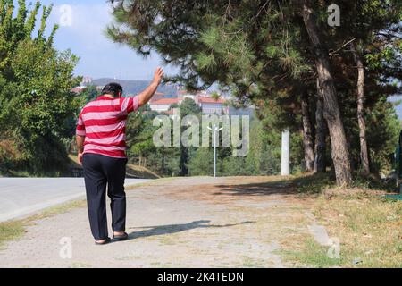 The man who raises his hand to say goodbye. The man who said goodbye and walked away. The old man walking in slippers. Stock Photo