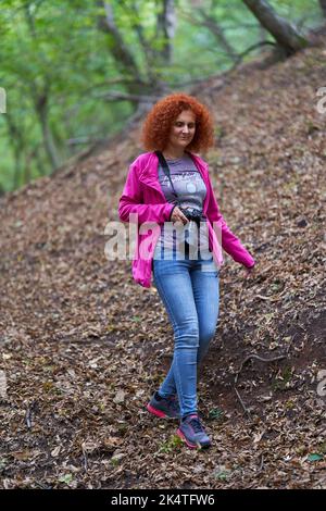 Photographer redhead curly hair woman hiking in the forest with her ...
