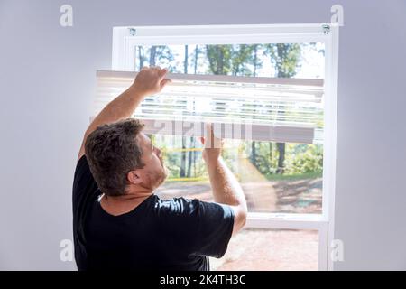 In a newly constructed house, a contractor is installing window blinds Stock Photo