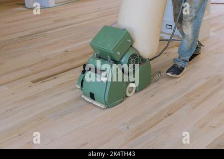 Using a floor sander, a new homeowner grinds a wooden parquet floor in a newly constructed home, using the sanding wheel as the tool Stock Photo