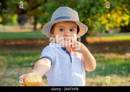 Generous child during picnic in the park offers his bitten apple with kindness. Stock Photo