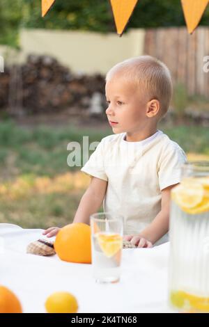 The child looks away, on the street. The child is a blue-eyed blonde, in a light yellow T-shirt. There are oranges and bright yellow shades on the bac Stock Photo
