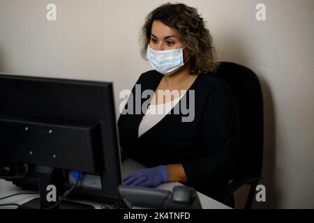 A call center agent working on the support hotline in the office, wearing a mask and gloves. The call center operator is talking to the customer. Clos Stock Photo