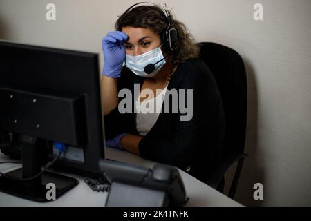 A call center agent working on the support hotline in the office, wearing a mask and gloves. The call center operator is talking to the customer. Clos Stock Photo