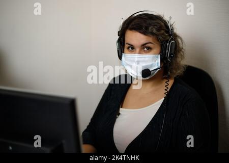 A call center agent working on the support hotline in the office, wearing a mask and gloves. The call center operator is talking to the customer. Clos Stock Photo