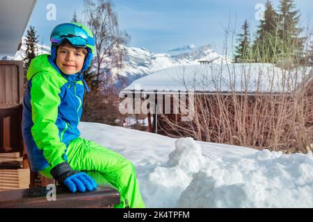 Young boy in ski outfit sit on balcony rail at winter vacations Stock Photo