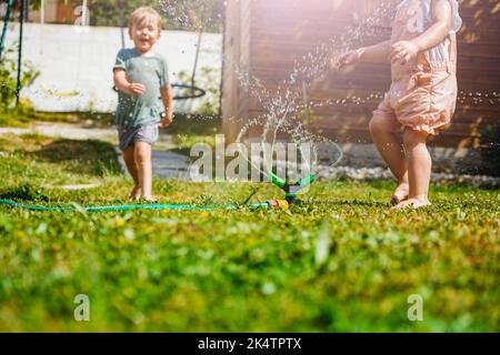 Boy and girl have fun in the garden - playing with water on lawn Stock Photo