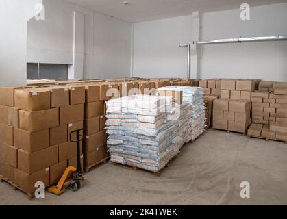 A pile of craft boxes and bags stacked on top of each other and a moving dolly in a white warehouse Stock Photo