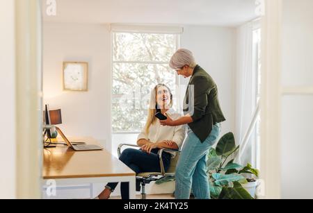 Happy young businesswoman showing her colleague her smartphone screen in a modern office. Two cheerful young businesswomen collaborating on a new task Stock Photo