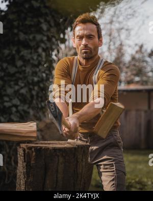Man in brown clothes is chopping wood with an axe Stock Photo