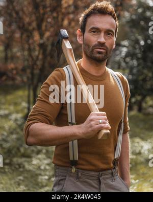 Handsome man with axe in brown clothes standing outside Stock Photo
