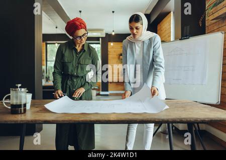 Innovative Muslim architects working on blueprint drawings in a modern office. Two businesswomen planning a new creative project. Two female designers Stock Photo