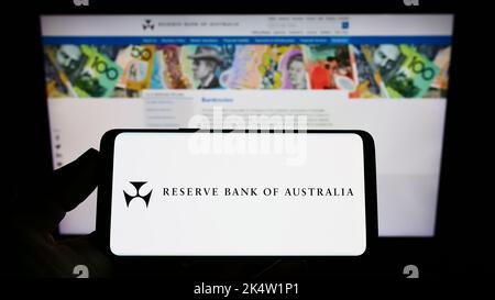 Person holding smartphone with logo of issuer Reserve Bank of Australia (RBA) on screen in front of website. Focus on phone display. Stock Photo