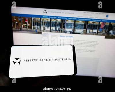Person holding mobile phone with logo of issuer Reserve Bank of Australia (RBA) on screen in front of web page. Focus on phone display. Stock Photo