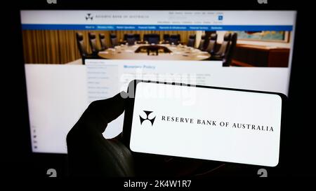 Person holding cellphone with logo of issuer Reserve Bank of Australia (RBA) on screen in front of business webpage. Focus on phone display. Stock Photo