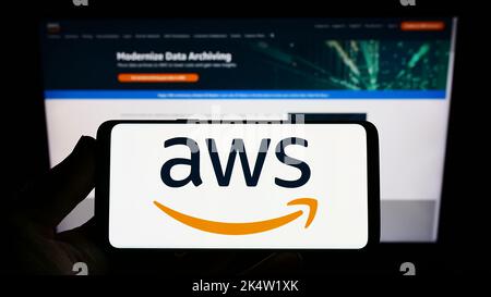 Person holding smartphone with logo of US cloud company Amazon Web Services Inc. (AWS) on screen in front of website. Focus on phone display. Stock Photo