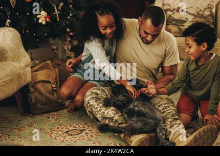 Happy military family playing with their cat at Christmas. Military dad reuniting with his children at home. Soldier spending quality time with his fa Stock Photo