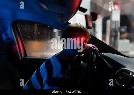 Tired Caucasian woman sits in car with head resting on steering wheel waiting for fellow traveler Stock Photo