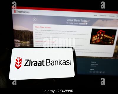 Person holding smartphone with logo of Turkish financial services company Ziraat Bank on screen in front of website. Focus on phone display. Stock Photo