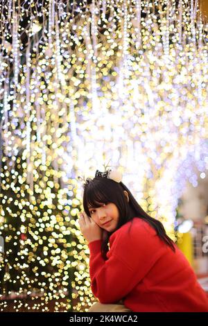 Beautiful Asian young woman with a red sweater with Christmas tree light Stock Photo