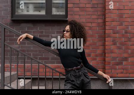 Portrait of a beautiful girl with curly hair standing against brick wall Stock Photo