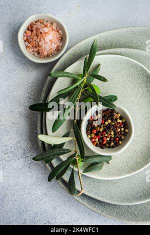 Overhead view of an olive branch, pink himalayan salt and mixed peppercorns on a stack of ceramic plates Stock Photo