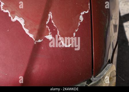 Weather damaged car hood paint coat. Peeling sun damaged paint surface in a 15 year old compact red car. Stock Photo