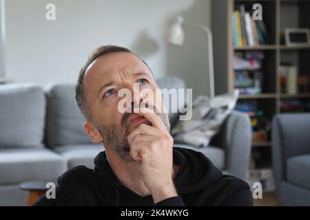 Man wondering expression at home. Looking up, hand on chin. Adult caucasian man in 30s or 40s concentrated and thinking. Stock Photo