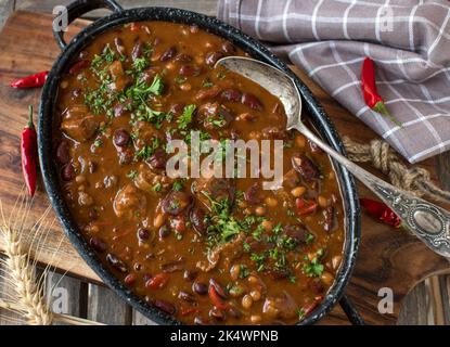 Chili con carne with meat cubes in a rustic pot on wooden table Stock Photo