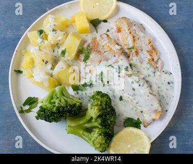 Pan fried natural fish fillet with broccoli, boild potatoes and herb, bechamel sauce on a plate Stock Photo