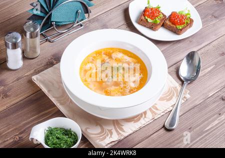 Fish soup - Russian fish soup with sandwiches with red caviar in a plate on a dark wooden background. Stock Photo