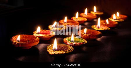 Diwali. Deepavali Hindu festival of lights. Clay diya candles in rows. Oil lamp lit on dark background Stock Photo