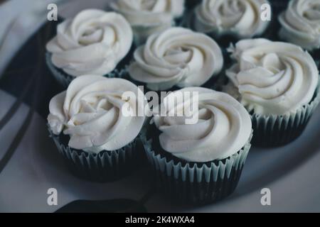 Bunch of delicious chocolate cupcakes with vanilla white cream topping on white serving plate. Selective focus. Stock Photo