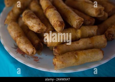 Delicious and crunchy vegetable spring rolls AKA Filipino vegetarian lumpia on white plate on blue tablecloth. Selective focus. Stock Photo