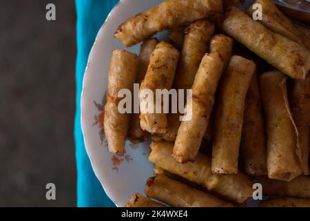 Flat lay shot of delicious and crunchy vegetable spring rolls AKA Filipino vegetarian lumpia on white plate on blue tablecloth. Selective focus. Stock Photo